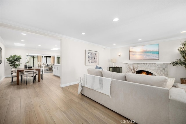 living room with a warm lit fireplace, baseboards, light wood-style flooring, crown molding, and recessed lighting