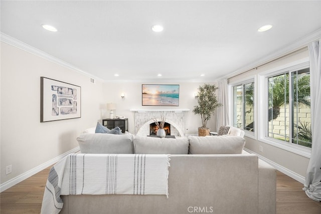 living room with recessed lighting, wood finished floors, a warm lit fireplace, ornamental molding, and baseboards