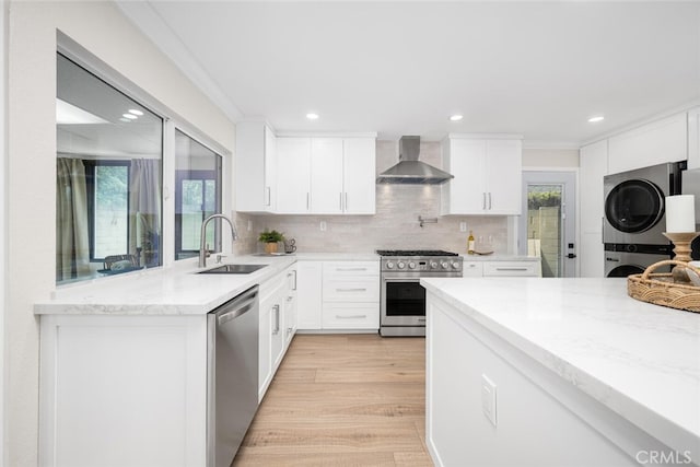 kitchen with wall chimney exhaust hood, light wood-style flooring, stainless steel appliances, stacked washing maching and dryer, and a sink