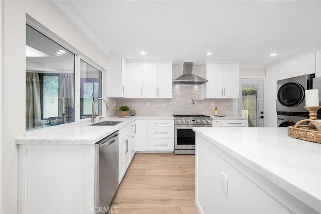 kitchen with stacked washer and dryer, stainless steel appliances, backsplash, a sink, and wall chimney exhaust hood