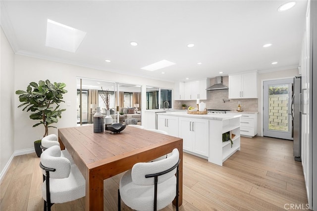 kitchen with light wood-type flooring, a skylight, light countertops, and wall chimney range hood