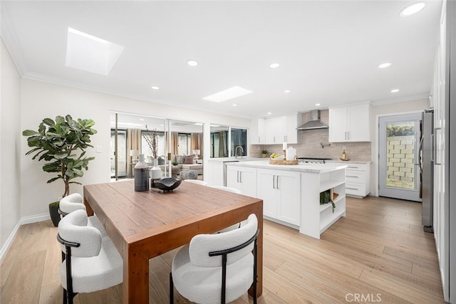 dining space with crown molding, light wood-style floors, baseboards, recessed lighting, and a skylight