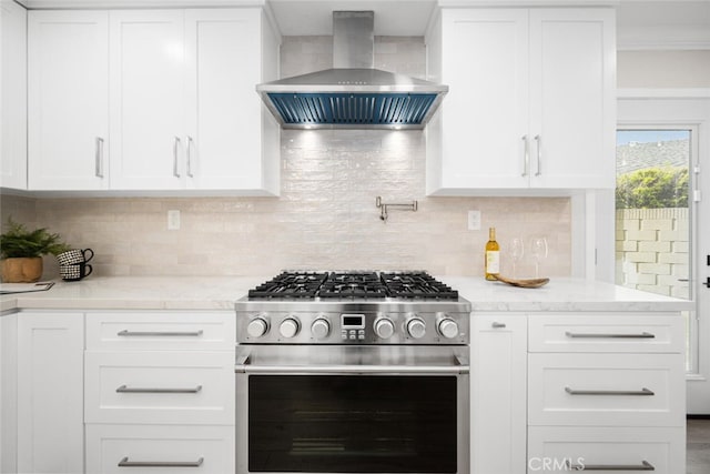 kitchen with tasteful backsplash, high end stainless steel range oven, white cabinetry, light stone countertops, and wall chimney exhaust hood