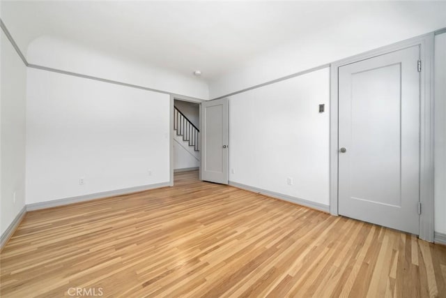 spare room with stairs, light wood-type flooring, and baseboards