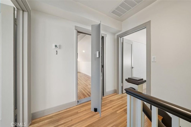 hall with an upstairs landing, visible vents, light wood finished floors, and baseboards