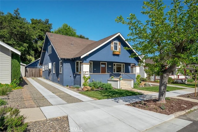 view of front of home with a shingled roof, a porch, and stucco siding