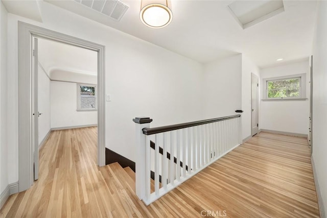 hall with visible vents, an upstairs landing, baseboards, and light wood finished floors