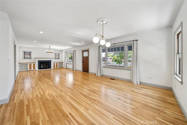 unfurnished living room with an inviting chandelier, baseboards, and light wood-type flooring