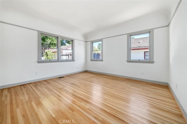 empty room featuring visible vents, light wood-type flooring, and baseboards