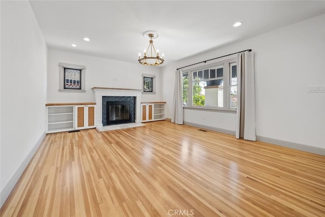 unfurnished living room with baseboards, a chandelier, light wood-type flooring, a premium fireplace, and recessed lighting