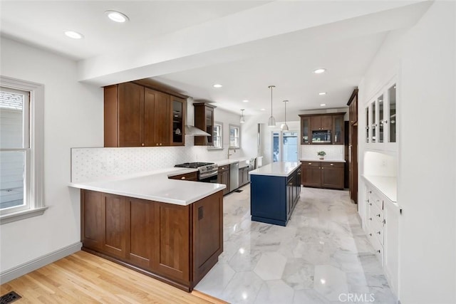 kitchen with a peninsula, light countertops, glass insert cabinets, appliances with stainless steel finishes, and backsplash