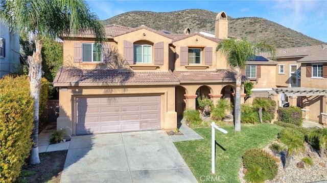 mediterranean / spanish home featuring a front lawn, a tiled roof, stucco siding, driveway, and an attached garage