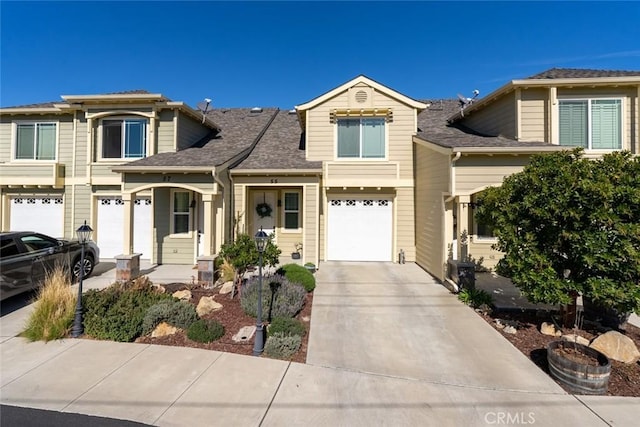 view of property with a garage, concrete driveway, and roof with shingles