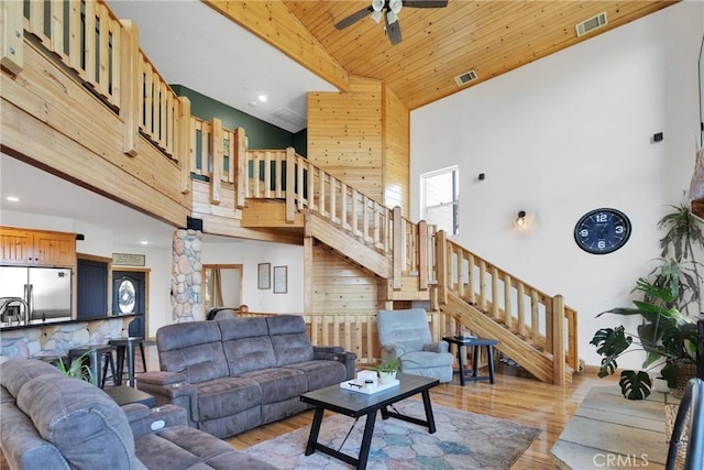 living area with beam ceiling, light wood finished floors, visible vents, a towering ceiling, and stairway