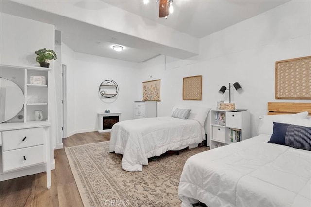 bedroom with a ceiling fan, a fireplace, and wood finished floors