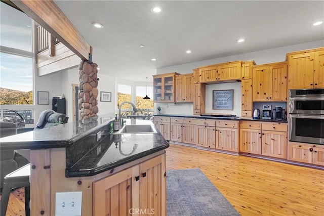 kitchen with light wood finished floors, glass insert cabinets, stainless steel double oven, a sink, and recessed lighting