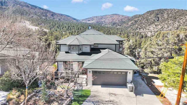 view of front of house with a shingled roof, concrete driveway, a mountain view, a garage, and a forest view