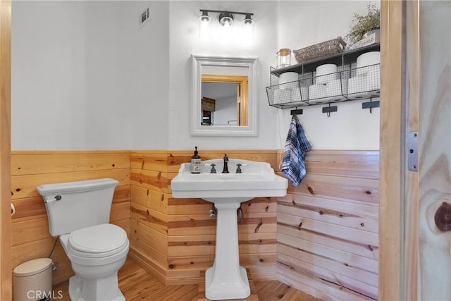 bathroom with toilet, wooden walls, visible vents, and wainscoting