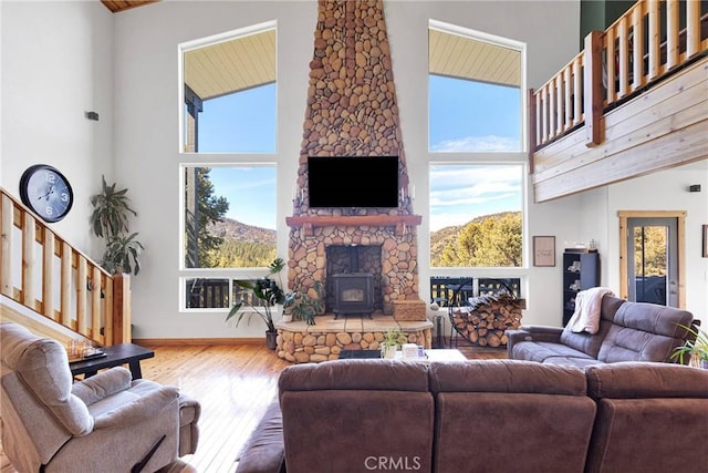 living area with a wood stove, a towering ceiling, baseboards, and wood finished floors