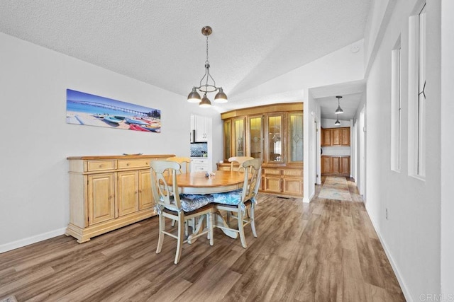 dining space featuring vaulted ceiling, a textured ceiling, baseboards, and wood finished floors