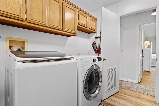 washroom featuring visible vents, baseboards, washer and clothes dryer, light wood-type flooring, and cabinet space