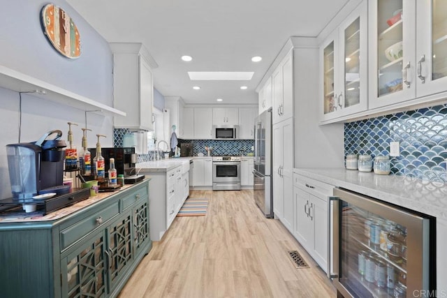 kitchen with light wood-type flooring, backsplash, white cabinetry, wine cooler, and appliances with stainless steel finishes