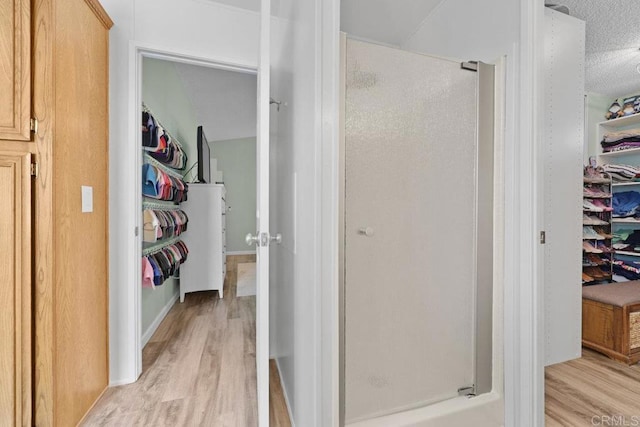 bathroom featuring a spacious closet, wood finished floors, a stall shower, and a textured ceiling