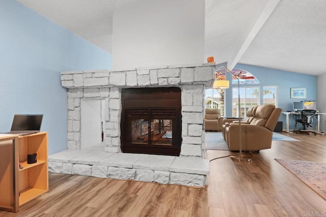 living area featuring a stone fireplace, lofted ceiling with beams, wood finished floors, and a textured ceiling