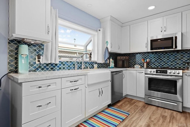 kitchen featuring backsplash, stainless steel appliances, light wood-style floors, and white cabinetry