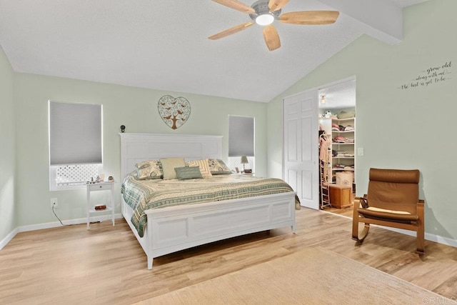 bedroom featuring a walk in closet, baseboards, lofted ceiling with beams, light wood-style floors, and a closet