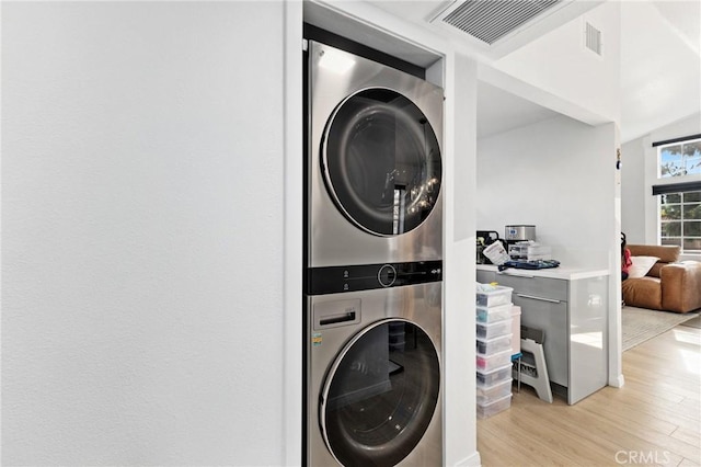 clothes washing area with laundry area, light wood-type flooring, stacked washer and clothes dryer, and visible vents