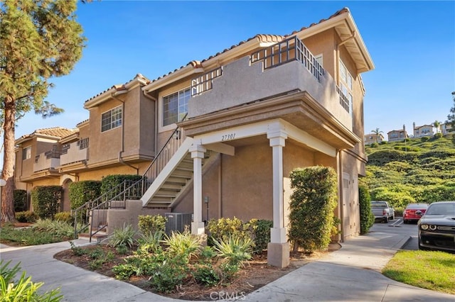 view of side of property featuring a tile roof, stairway, and stucco siding