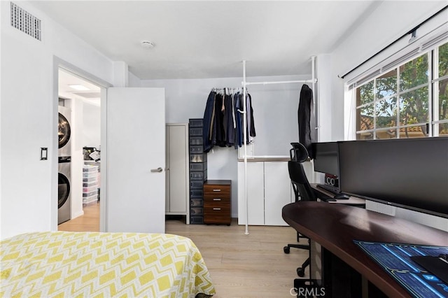 bedroom featuring visible vents, stacked washer / dryer, and wood finished floors