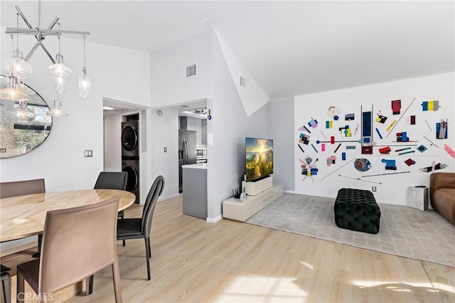 dining space with stacked washer and dryer, visible vents, high vaulted ceiling, and light wood-style flooring