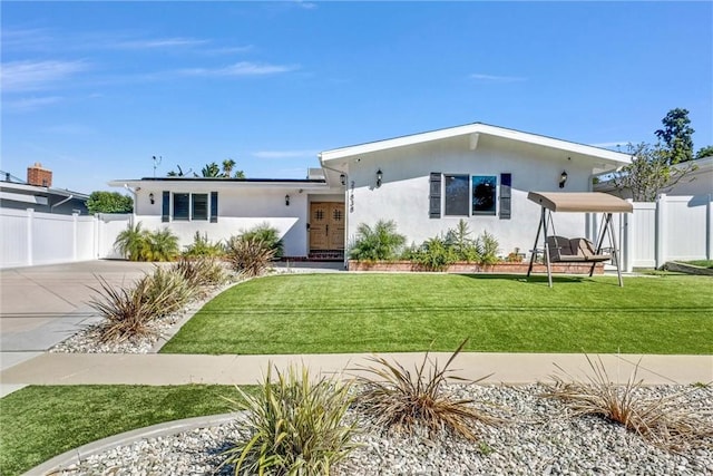 view of front of property featuring solar panels, stucco siding, concrete driveway, fence, and a front lawn