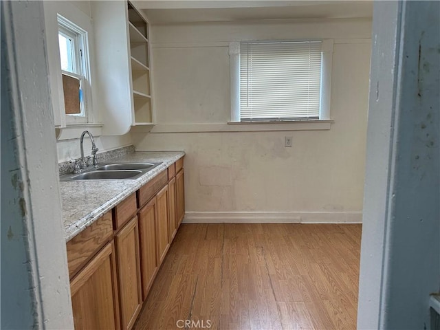 kitchen with open shelves, light countertops, light wood-style floors, brown cabinetry, and a sink