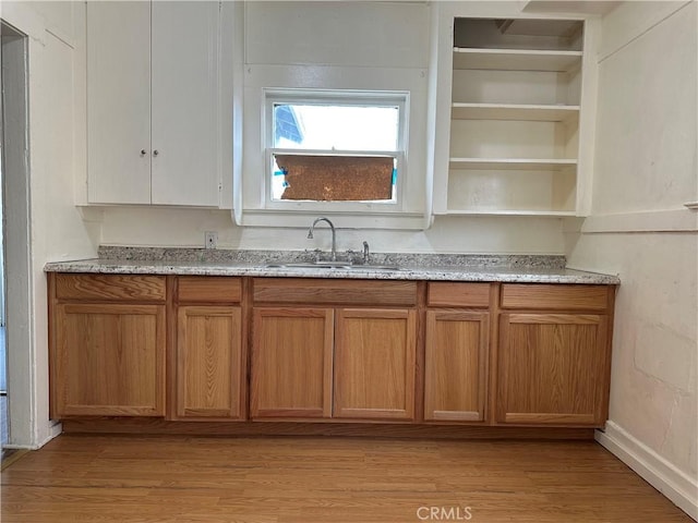 kitchen featuring brown cabinetry, light stone countertops, light wood-style floors, open shelves, and a sink