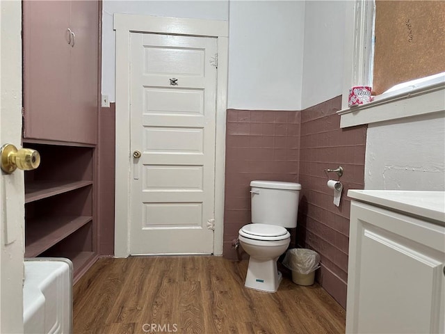 bathroom featuring toilet, a wainscoted wall, wood finished floors, vanity, and tile walls