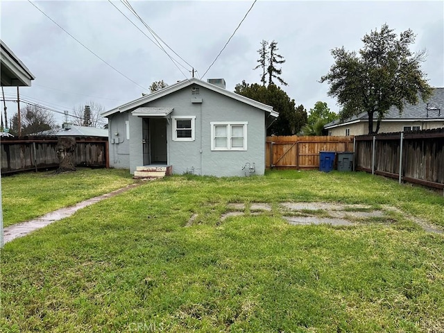 back of house featuring a fenced backyard, a yard, and stucco siding