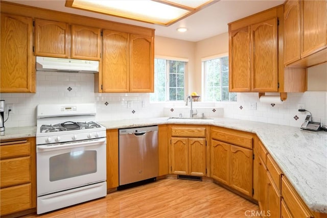 kitchen with under cabinet range hood, a sink, stainless steel dishwasher, white gas range oven, and light wood finished floors