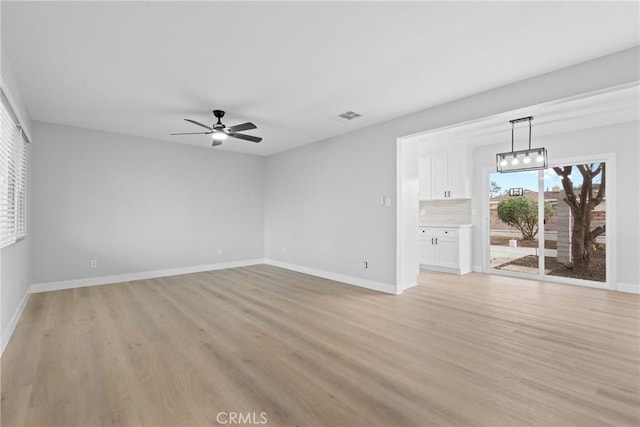 unfurnished room with light wood-type flooring, visible vents, baseboards, and ceiling fan with notable chandelier