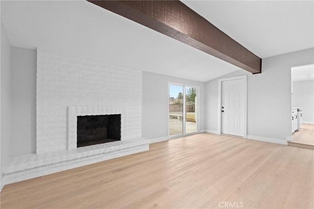 unfurnished living room with lofted ceiling with beams, light wood-type flooring, a brick fireplace, and baseboards