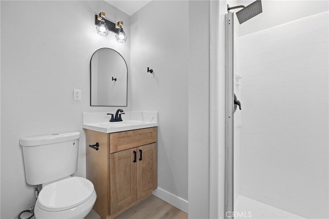 bathroom featuring toilet, wood finished floors, vanity, baseboards, and tiled shower