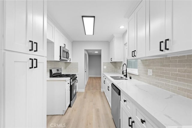 kitchen with stainless steel appliances, a sink, white cabinetry, light wood-style floors, and light stone countertops