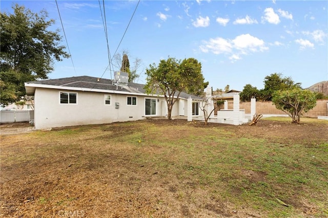 back of house featuring stucco siding, fence, and a lawn