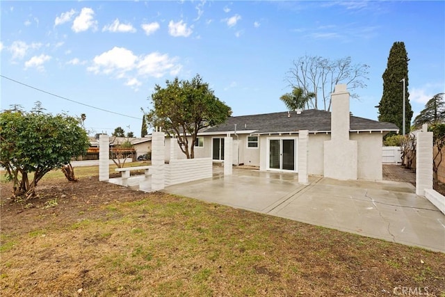 rear view of house with a patio area, a chimney, fence, and stucco siding