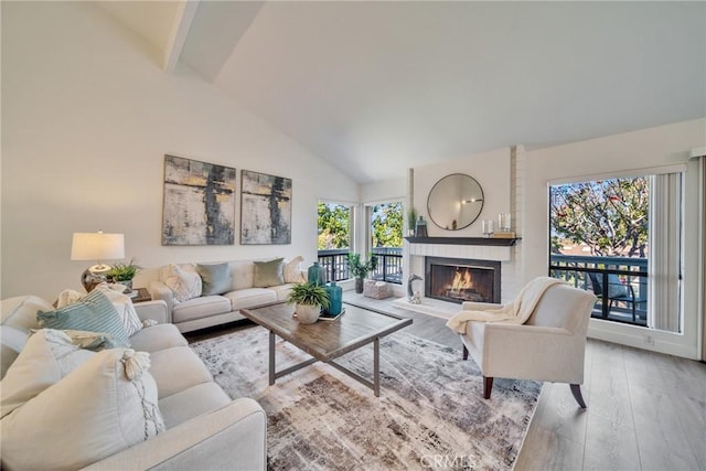 living area featuring high vaulted ceiling, plenty of natural light, wood finished floors, and a brick fireplace