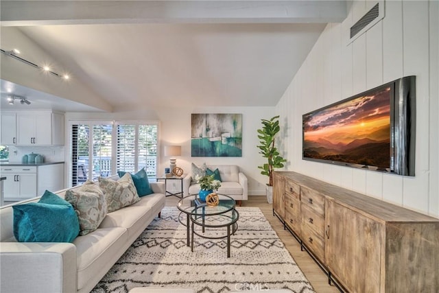 living area with a fireplace, visible vents, vaulted ceiling with beams, and light wood finished floors