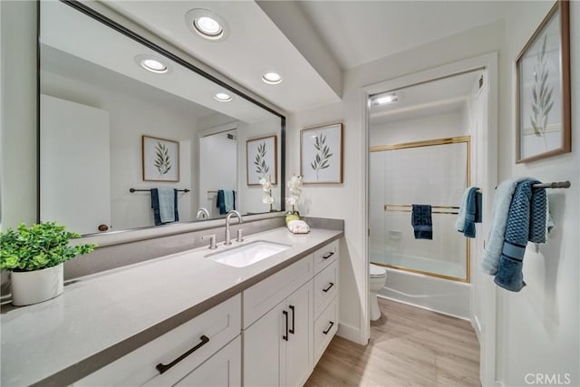 bathroom featuring bath / shower combo with glass door, recessed lighting, toilet, vanity, and wood finished floors