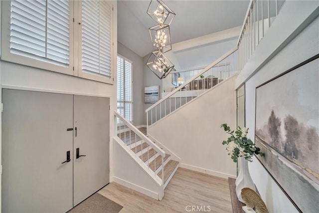 entryway featuring baseboards, stairway, wood finished floors, and an inviting chandelier